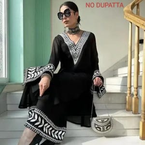 May include: Black ensemble with white embroidered leaf patterns on the sleeves and pants. The outfit includes a V-neck top and wide-leg pants. A small, beaded purse is held in the hand. The text "NO DUPATTA" is visible in the background.