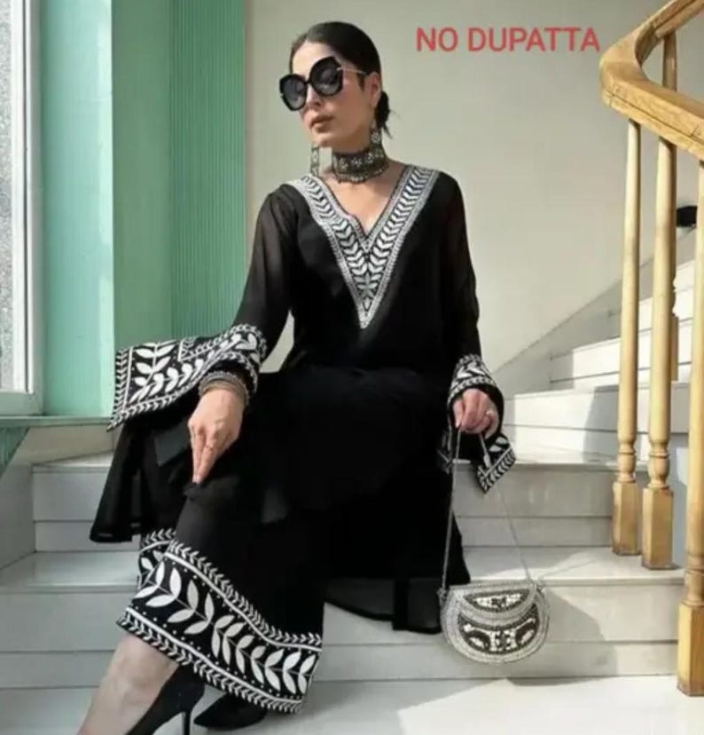 May include: Black ensemble with white embroidered leaf patterns on the sleeves and pants. The outfit includes a V-neck top and wide-leg pants. A small, beaded purse is held in the hand. The text "NO DUPATTA" is visible in the background.