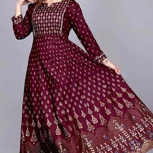 May include: A maroon maxi dress with a gold floral print and a V-neckline. The dress has long sleeves and a flowing skirt.