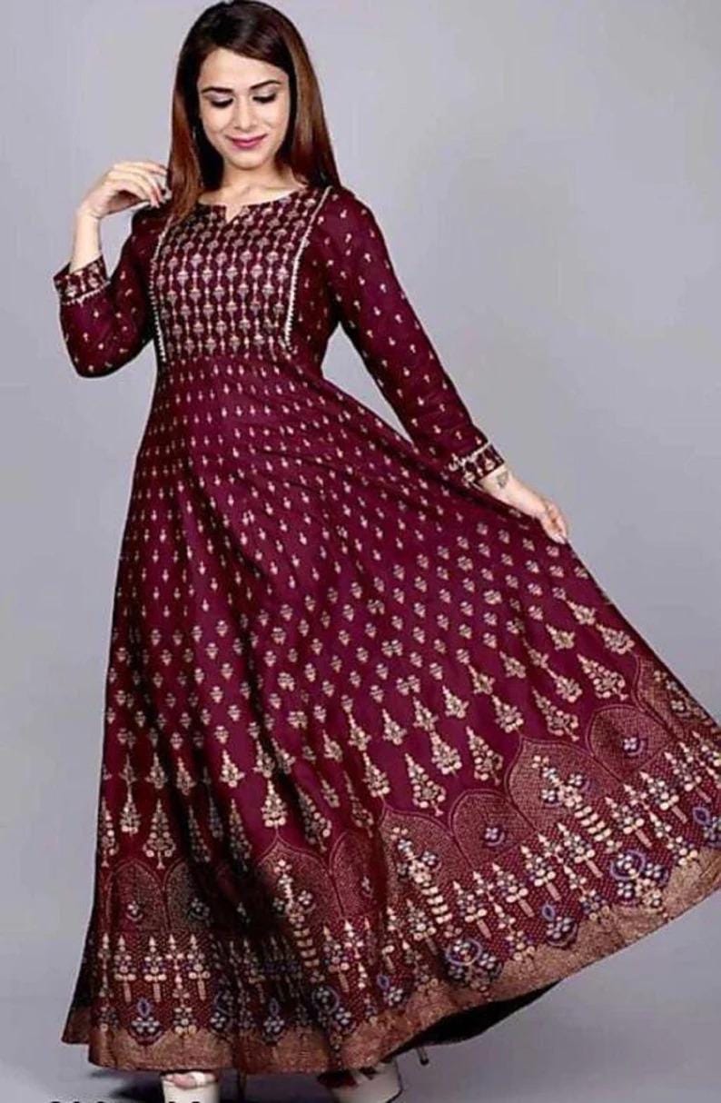 May include: A maroon maxi dress with a gold floral print and a V-neckline. The dress has long sleeves and a flowing skirt.