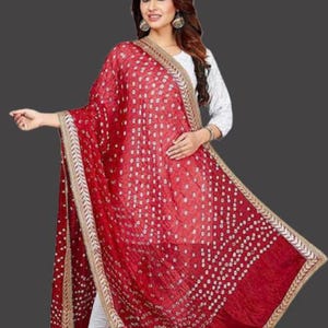 May include: A vibrant red dupatta with a white dotted pattern and gold trim. The scarf is draped, showcasing its flowing fabric and intricate design. This traditional Indian garment adds a touch of elegance.