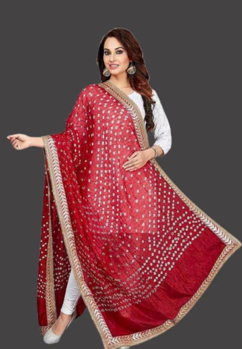 May include: A vibrant red dupatta with a white dotted pattern and gold trim. The scarf is draped, showcasing its flowing fabric and intricate design. This traditional Indian garment adds a touch of elegance.