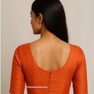 Könnte beinhalten: Eine orangefarbene Bluse mit kurzen Ärmeln und einem Rundhalsausschnitt. Die Rückseite der Bluse hat eine Reihe kleiner Knöpfe in der Mitte. Der Text "TrishanFashionHub" ist unten auf der Bluse zu sehen.