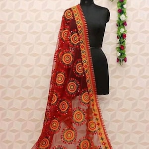 May include: A red sheer shawl with intricate embroidery in yellow and black. The shawl features a circular pattern with sequins and beads.