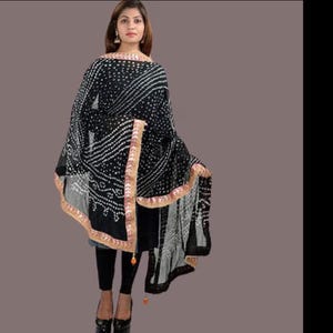 May include: A black and white patterned shawl with a decorative border. The shawl is draped over a person wearing black leggings and shoes. The shawl has a detailed design with white dots and lines.