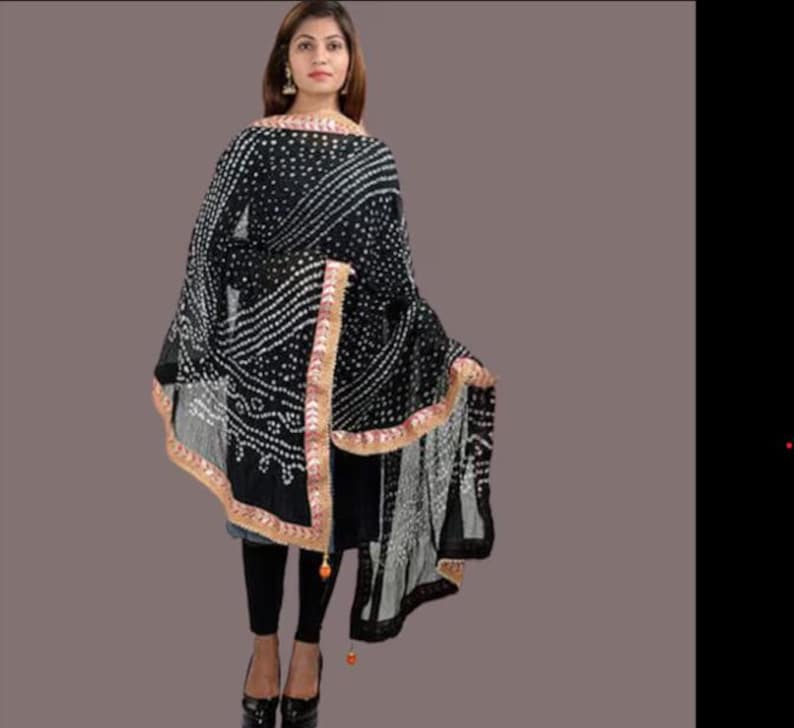 May include: A black and white patterned shawl with a decorative border. The shawl is draped over a person wearing black leggings and shoes. The shawl has a detailed design with white dots and lines.
