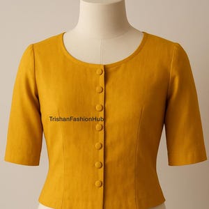 Puede incluir: Blusa amarilla mostaza de manga corta con cuello redondo y cierre de botones. La blusa se exhibe en un maniquí. El texto "TrishanFashionHub" está impreso en la parte delantera de la blusa.