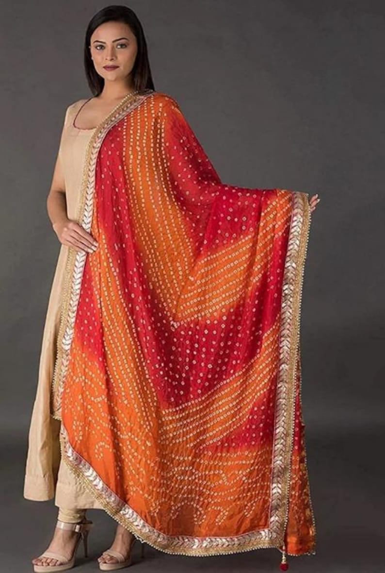 May include: A vibrant, patterned scarf in shades of red and orange, with a decorative border. The scarf features a detailed design and is likely made of a lightweight fabric. The scarf is a fashion accessory, suitable for adding a pop of color to an outfit.