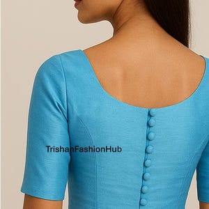 May include: A light blue blouse with short sleeves and a scoop neckline. The back of the blouse features a row of buttons. The text "TrishanFashionHub" is visible on the front of the blouse.