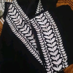 May include: Black garment with white leaf embroidery. The embroidery is detailed and runs along the edges of the garment. The fabric appears to be a lightweight material.