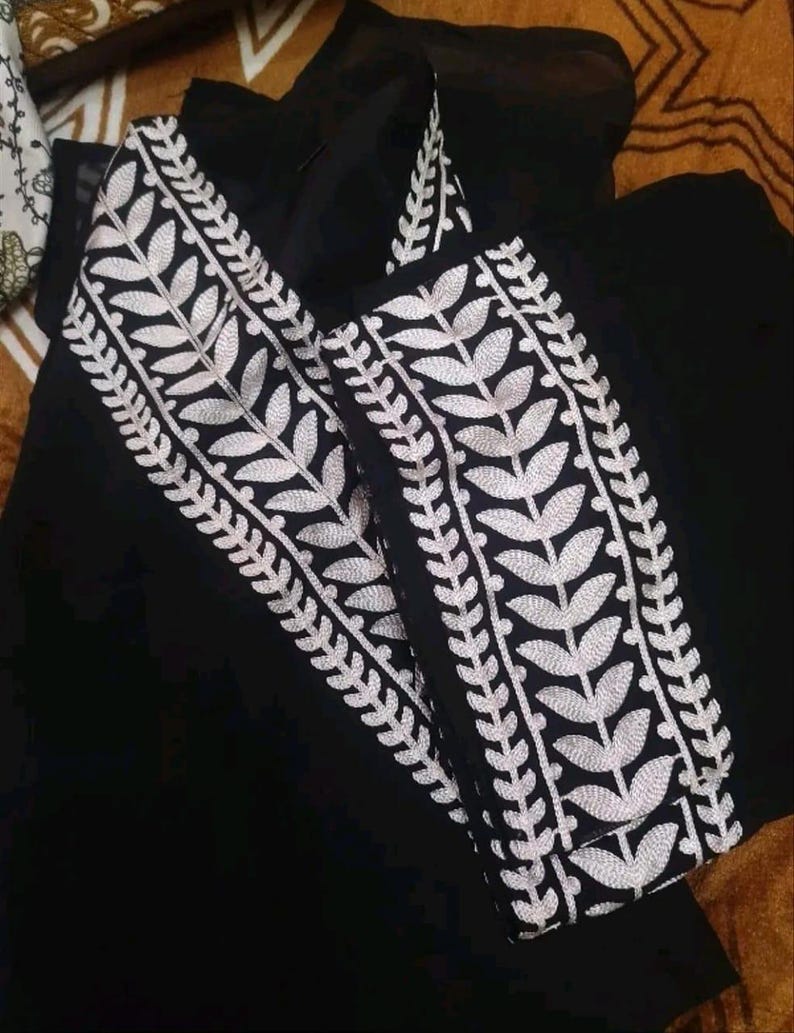 May include: Black garment with white leaf embroidery. The embroidery is detailed and runs along the edges of the garment. The fabric appears to be a lightweight material.