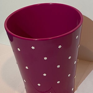 May include: A magenta ceramic planter with a white flower pattern. The planter is a tapered cylinder shape.