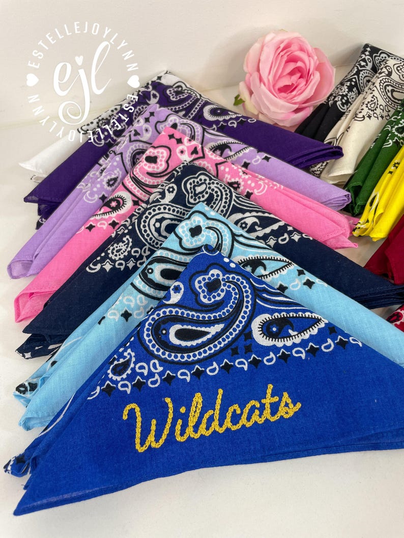 Puede incluir: Una colecci&oacute;n de pa&ntilde;uelos de algod&oacute;n doblados en varios colores, incluyendo azul real, azul claro, marino, rosa, morado y amarillo, todos con un patr&oacute;n de cachemira tradicional. El pa&ntilde;uelo azul real tiene la palabra Wildcats bordada en oro.
