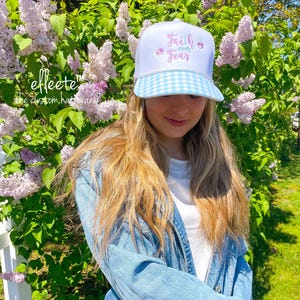 May include: White trucker hat with a light blue gingham brim. The hat features the text "Faith over Fear" in pink script with floral accents. The hat is part of the "effeete" custom hat brand.
