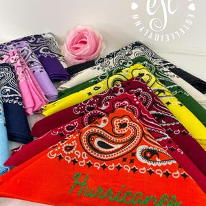 Puede incluir: Una colecci&oacute;n de pa&ntilde;uelos de algod&oacute;n doblados con patrones de cachemira tradicionales en varios colores, incluyendo naranja, rojo, granate, amarillo, verde, negro, rosa, morado y azul. El pa&ntilde;uelo naranja tiene bordada la palabra Hurricanes.