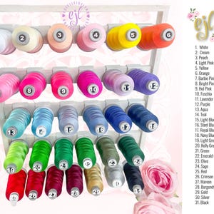 May include: A white rack with 31 spools of thread in various colors. The spools are numbered 1 through 31 and each color is labeled with a corresponding number and name. The colors include white, cream, peach, light pink, yellow, orange, barbie pink, bright pink, hot pink, fuchsia, lavender, purple, aqua, teal, light blue, steel blue, royal blue, navy blue, light green, kelly green, green, emerald green, olive, sage, red, crimson, maroon, burgundy, gold, silver, and black.