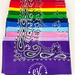 Puede incluir: Una pila de doce pa&ntilde;uelos cuadrados en varios colores, incluyendo blanco, negro, rojo, amarillo, verde, azul marino, azul, azul claro, rosa, lavanda y morado. Cada pa&ntilde;uelo presenta un patr&oacute;n de cachemira blanco tradicional y un logotipo central que dice ESTELLEJOYLYNN ejl.