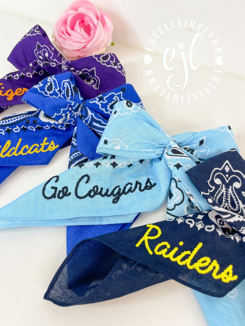 Puede incluir: Una colecci&oacute;n de cuatro lazos para el pelo de tela con estampado de bandana en tonos morado, azul real, azul claro y azul marino. Los lazos presentan texto bordado que incluye Tiger, Wildcats, Go Cougars y Raiders en amarillo o negro.