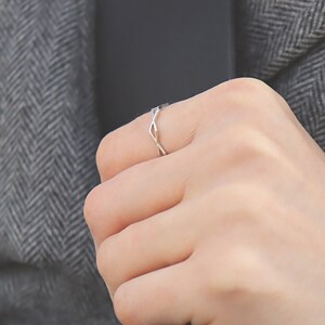 May include: A close-up of a hand wearing a thin silver ring. The ring is a simple band with a twisted design.