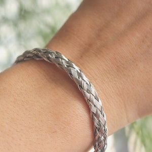 May include: A silver braided bracelet on a person's wrist.
