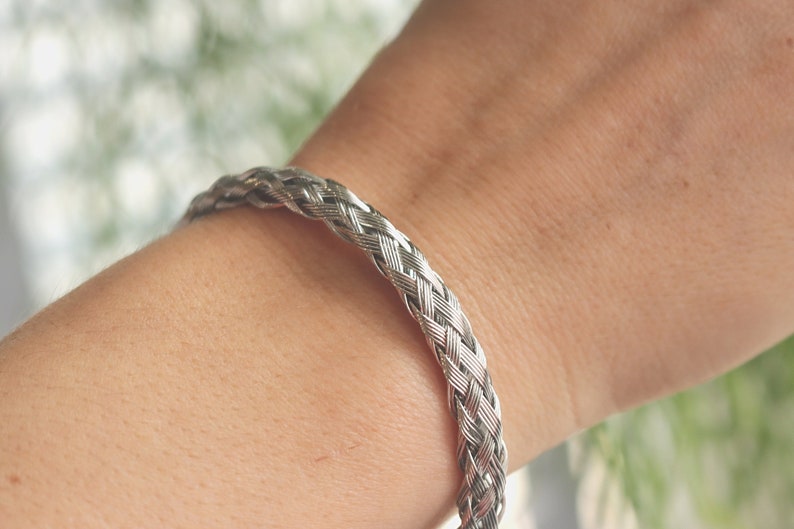 May include: A silver braided bracelet on a person's wrist.