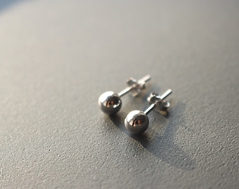May include: A pair of silver ball stud earrings. The earrings are small and round, with a simple design.