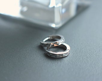 May include: A pair of silver hoop earrings with a geometric pattern. The earrings are on a gray surface.