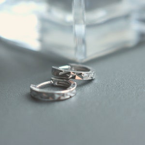 May include: A pair of silver hoop earrings with a textured design.