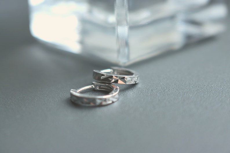 May include: A pair of silver hoop earrings with a textured design.