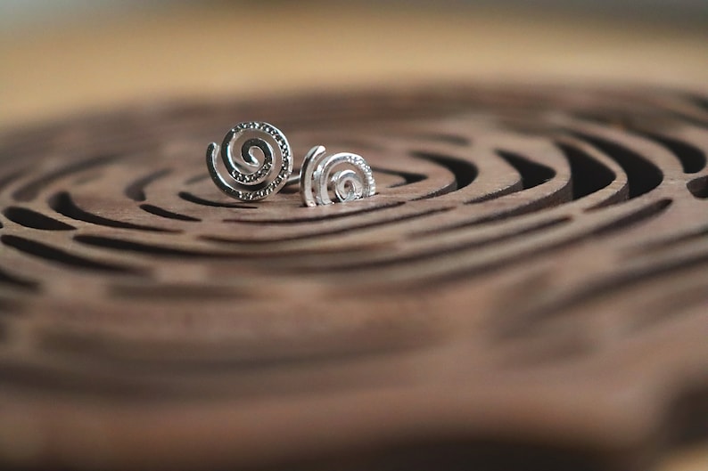 May include: A pair of silver spiral earrings on a wooden surface with a circular pattern.