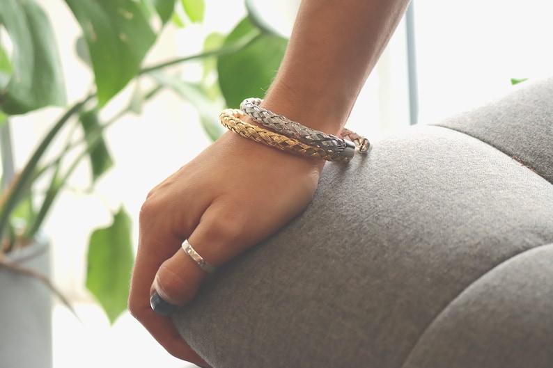 May include: Two braided bracelets, one gold and one silver, worn on a person's wrist.
