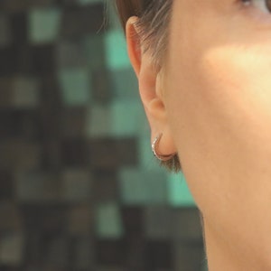 May include: A close-up of a person's ear with a small silver hoop earring. The earring is simple and understated, and it is a popular choice for both men and women.