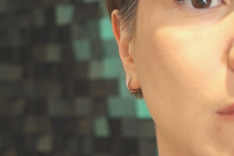 May include: A close-up of a person's ear with a small silver hoop earring. The earring is simple and understated, and it is a popular choice for both men and women.