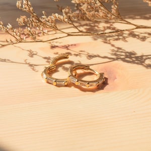 Peut inclure: Une paire de boucles d'oreilles créoles en or avec des pierres claires en forme de baguette serties autour des créoles.