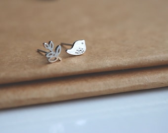 May include: A pair of silver stud earrings, one featuring a small bird design and the other a simple leaf design.