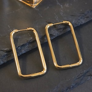 May include: A pair of gold rectangle hoop earrings. The earrings are made of a thick, smooth metal.