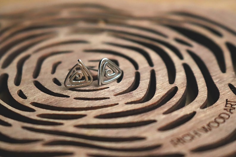 May include: A pair of silver triangle earrings with a spiral design. The earrings are on a wooden surface with a circular pattern.