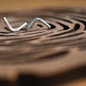 May include: Two silver-coloured metal pieces shaped like a letter V, lying on a brown wooden surface with a circular pattern.