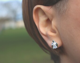May include: A close-up of a person's ear with a silver leaf-shaped earring. The earring is a simple design with a textured surface.
