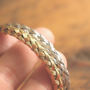 May include: A gold and silver braided bracelet, woven together in a tight pattern.