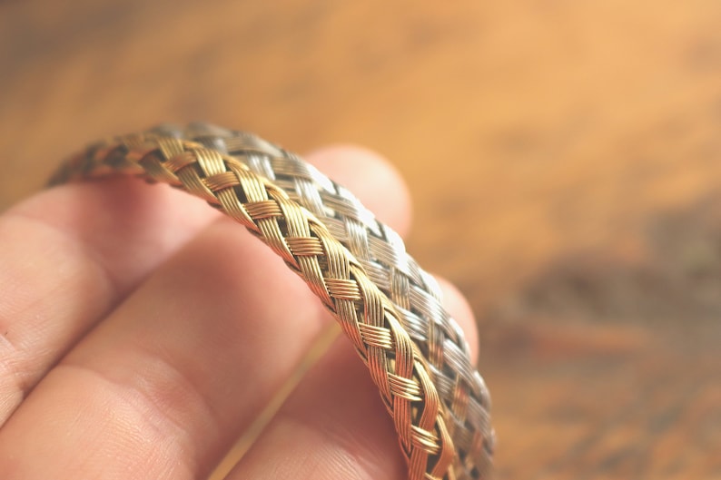 May include: A gold and silver braided bracelet, woven together in a tight pattern.