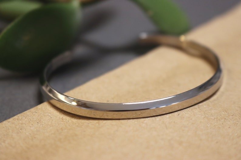 May include: A silver bangle bracelet with a smooth, rounded surface. The bracelet is made of metal and has a simple, elegant design.