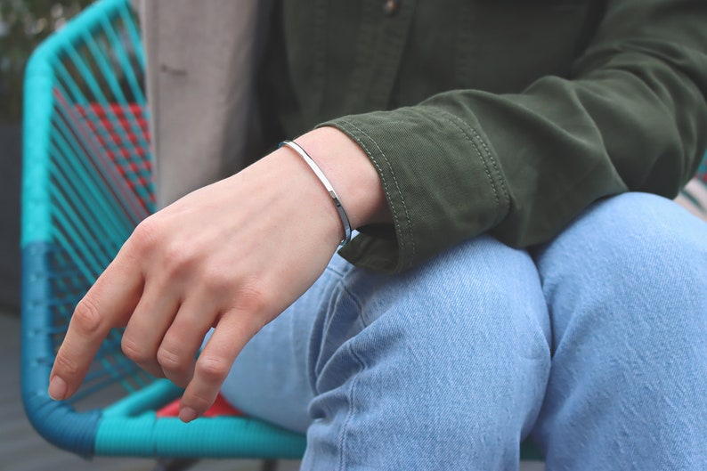May include: A silver bangle bracelet on a person's wrist. The bracelet is simple and sleek, with a polished finish.