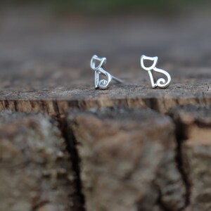 May include: A pair of silver cat-shaped stud earrings. The earrings are simple and delicate, with a minimalist design.