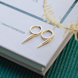Peut inclure: Une paire de boucles d'oreilles créoles en or avec un détail pointu et acéré suspendu à chaque créole.