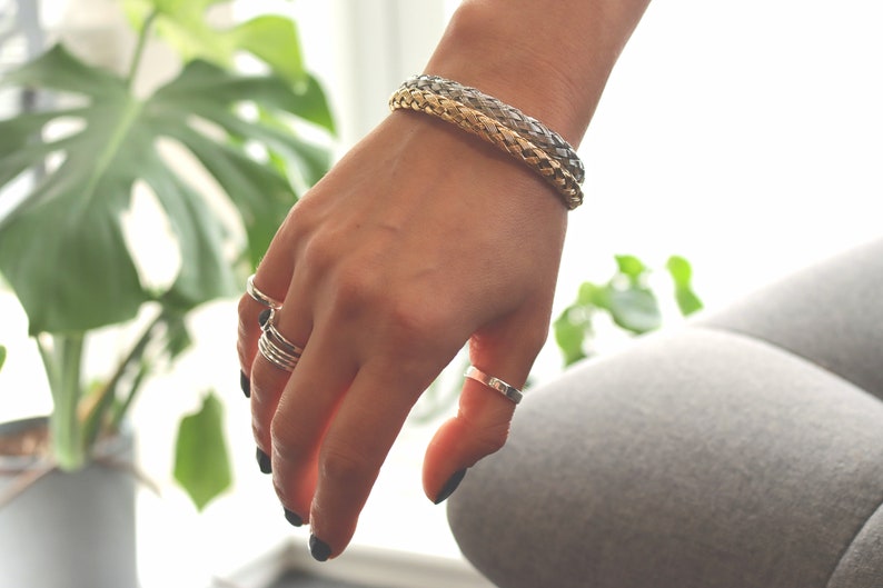 May include: A hand wearing a braided silver and gold bracelet and several silver rings.