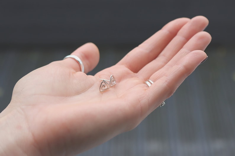 May include: A pair of silver triangle stud earrings with a spiral design.