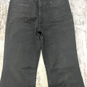 Może przedstawiać: Czarne dżinsy Wrangler z denimu z wysokim stanem i rozszerzaną nogawką. Dżinsy mają dwie przednie i dwie tylne kieszenie. Logo Wrangler jest widoczne na tylnej kieszeni. Dżinsy są wykonane z wytrzymałego denimu.