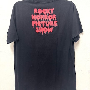 Puede incluir: Camiseta negra con un estampado gr&aacute;fico rojo de las palabras "Rocky Horror Picture Show" en letras que gotean.