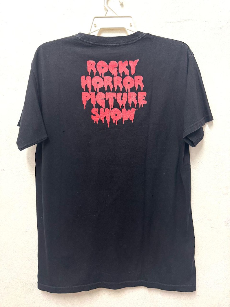 Puede incluir: Camiseta negra con un estampado gr&aacute;fico rojo de las palabras "Rocky Horror Picture Show" en letras que gotean.